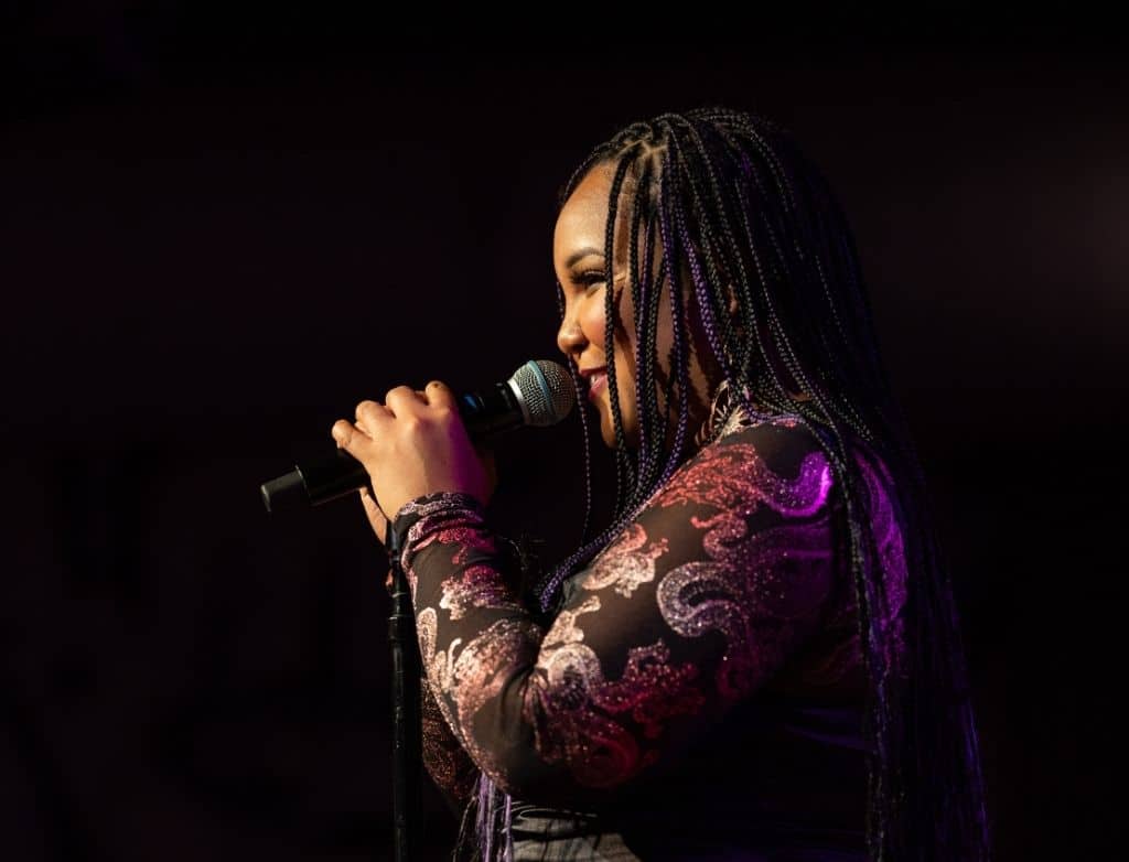 Alexis Lombre singing into a mic and smiling at the audience