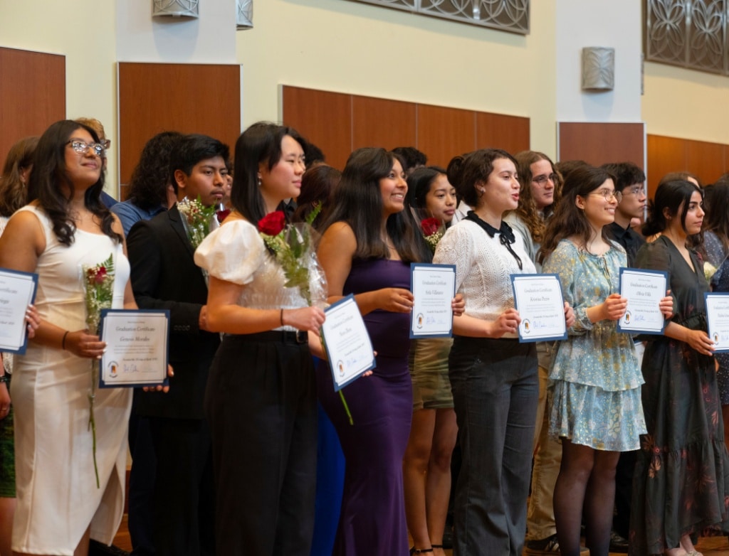 Students standing onstage with their diplomas.