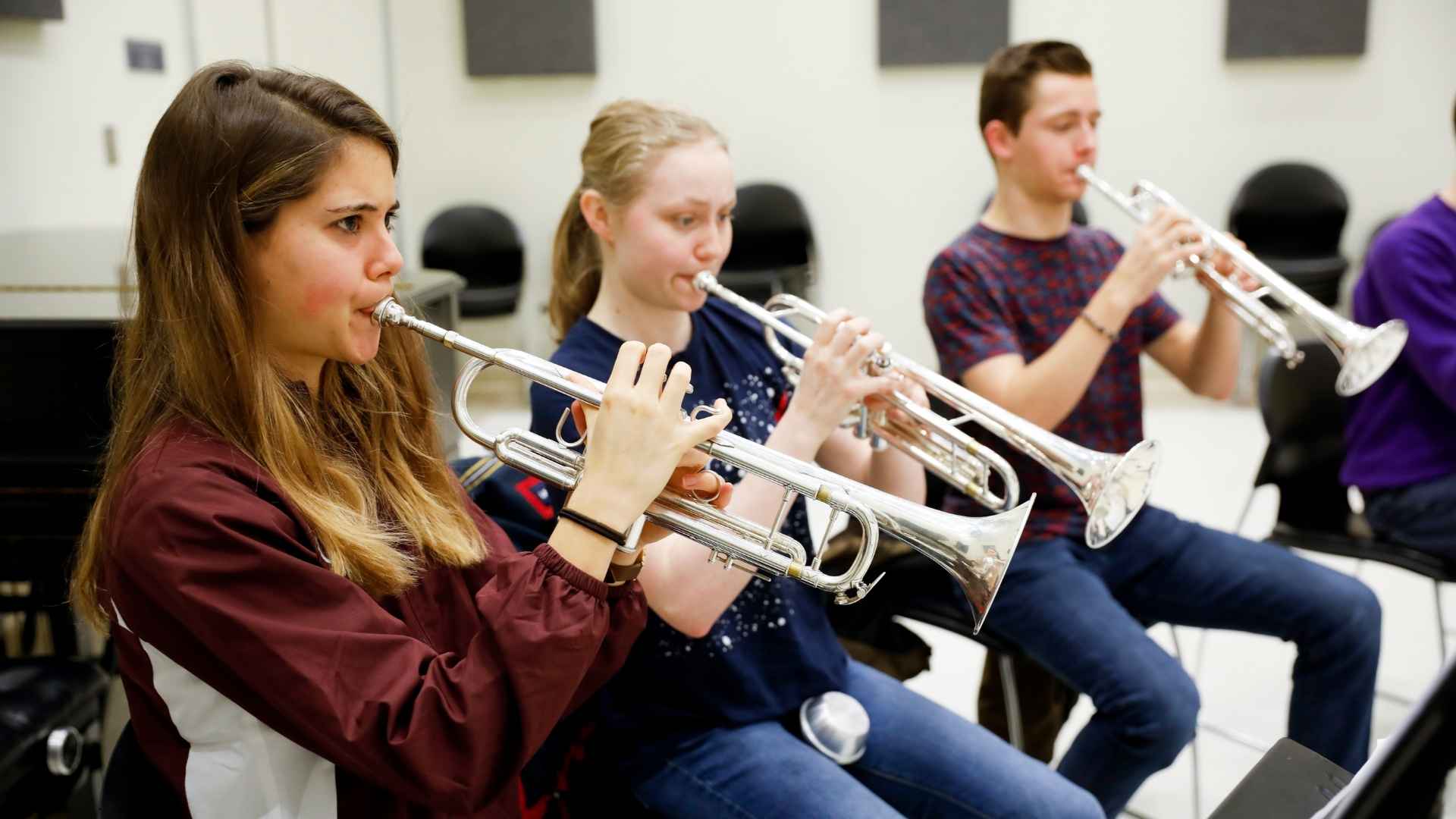 Three students are seated, playing trumpets.