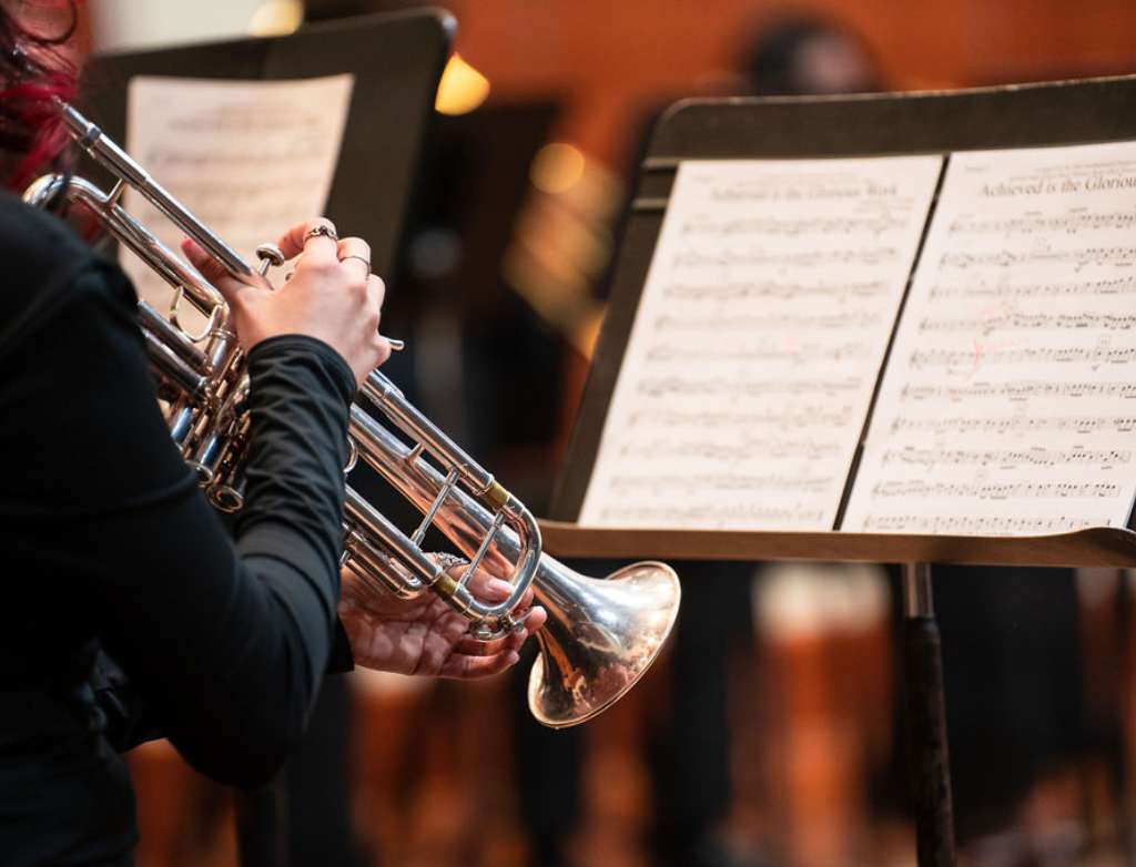 A trumpet student plays their instrument while reading sheet music