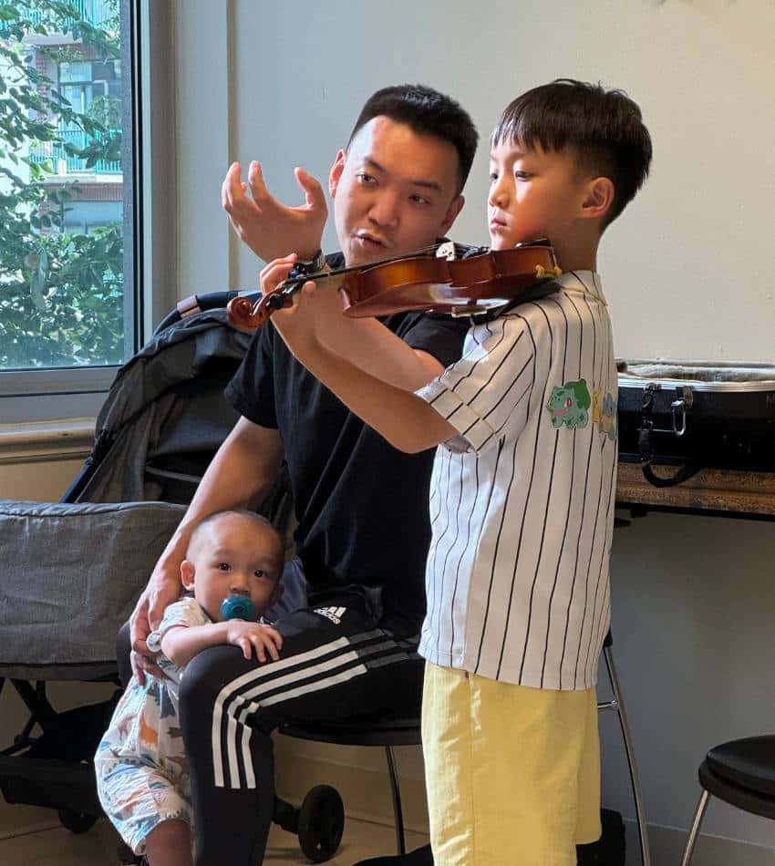 A parent corrects his son's violin hold.