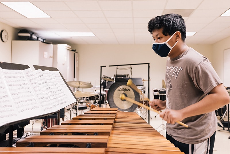 A student reading sheet music while playing the marimba