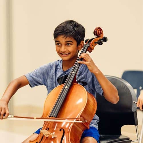 A music camp student plays the cello and smiles