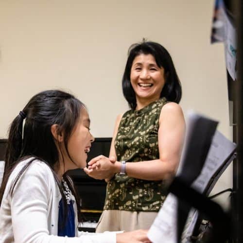 A music teacher and piano student laugh