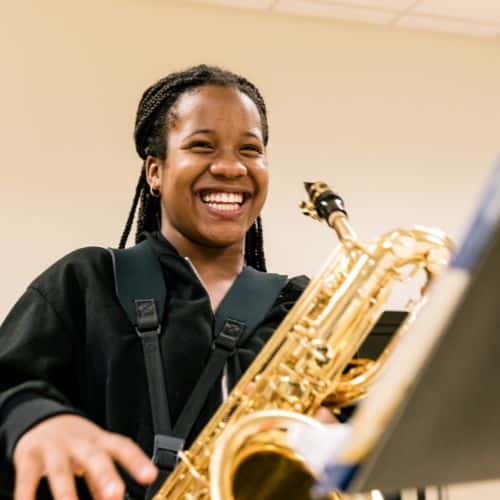 A music camp student laughs while playing the saxophone