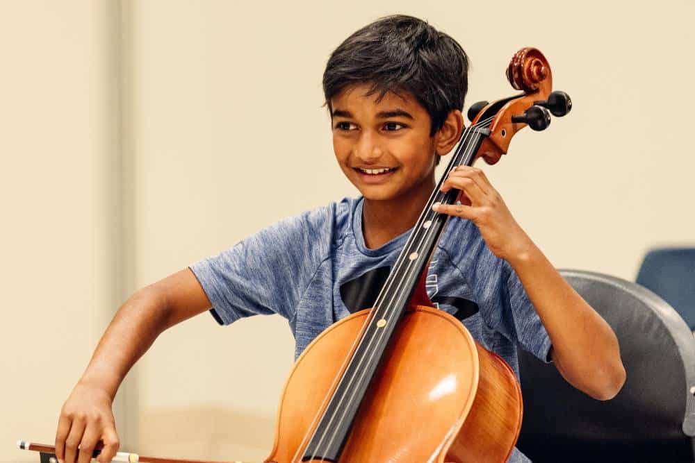 A music camp student plays the cello and smiles