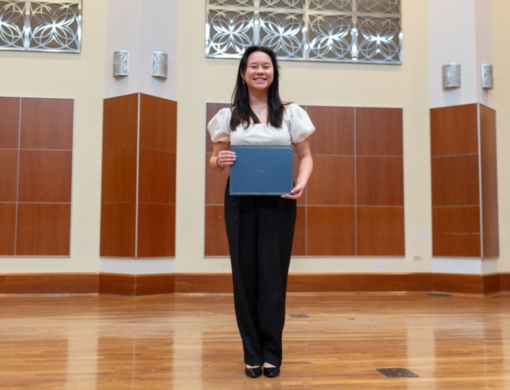 Nora Zhou holding a diploma onstage.