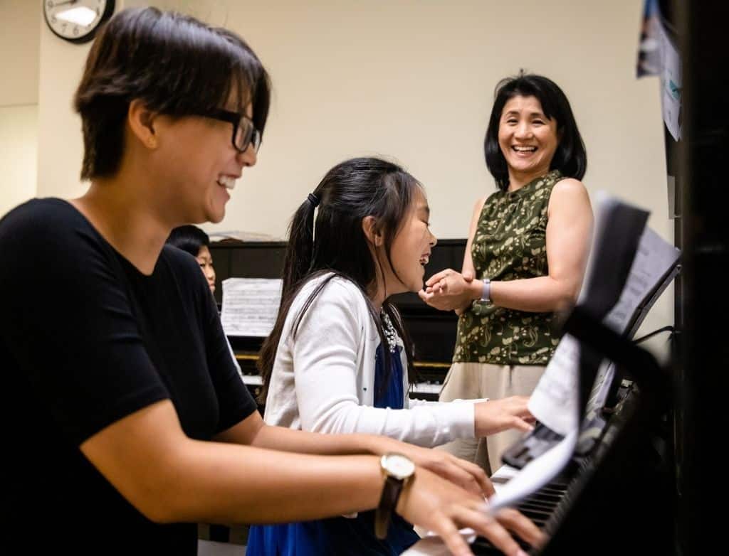 Two piano students laughing with their teacher