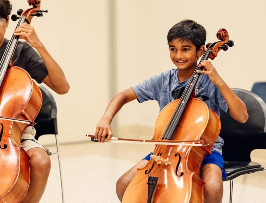A Suzuki Method student plays the cello and smiles