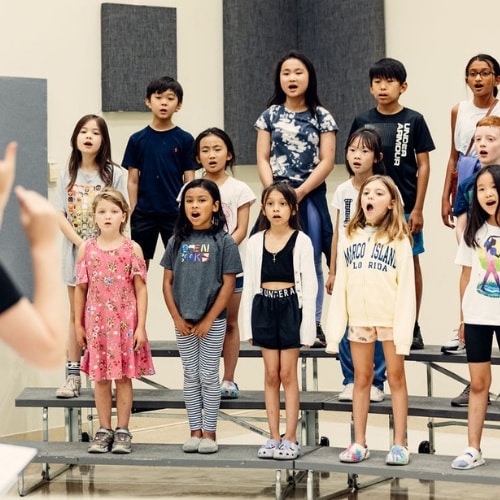 Choir students sing together as a group as their voice teacher directs them.