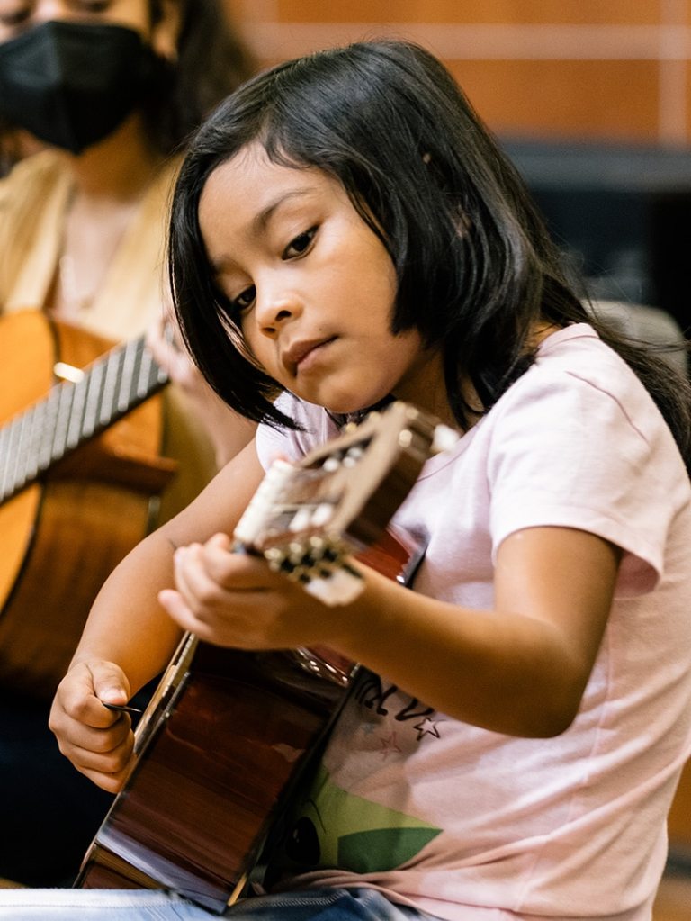 A young guitar student focusing on creating chords on the guitar frets