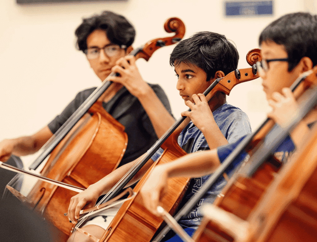 Three cello students sit in a line, playing.