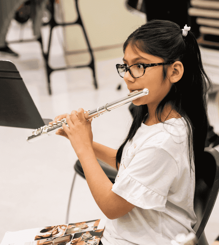 A choir of children sing together, standing on risers. In front of them is the ensemble director conducting.