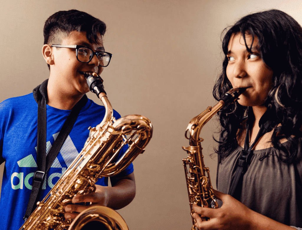 Two students are facing each other and smiling as they play saxophone.