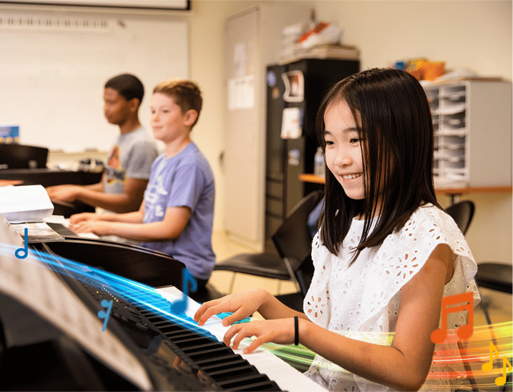 A young student smiles while playing a keyboard. In the background, two other students play.
