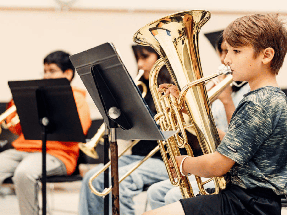 Four students playing brass instruments look at their music stands.