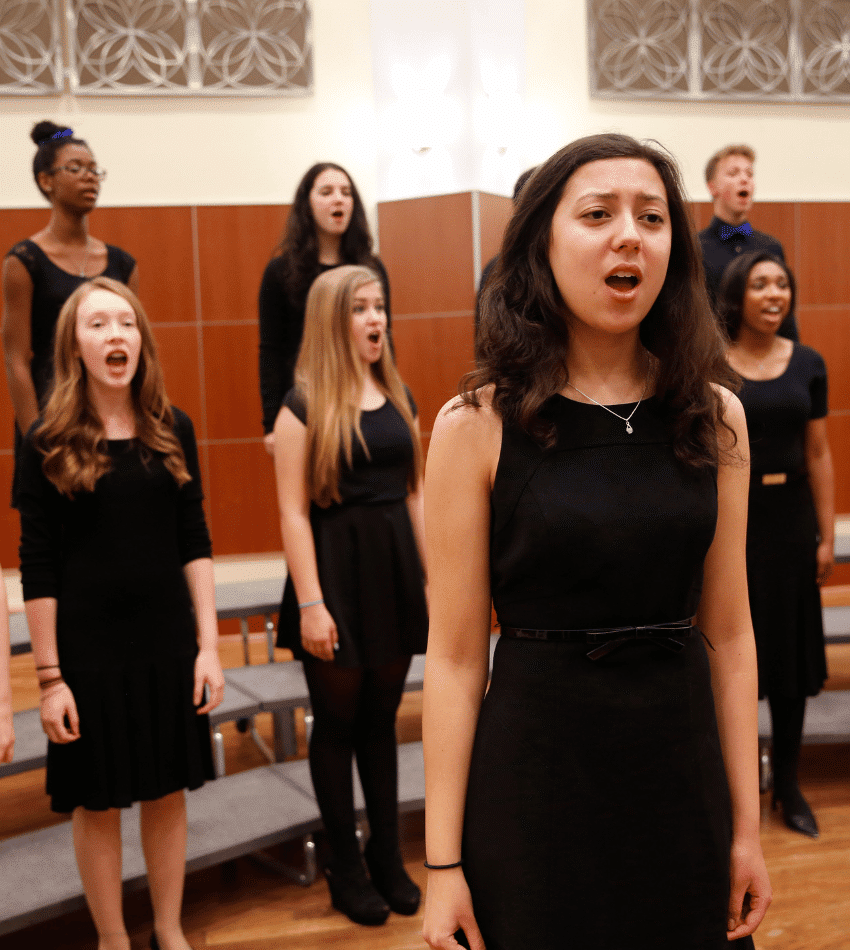 A student with a solo stands in front of a choir onstage.