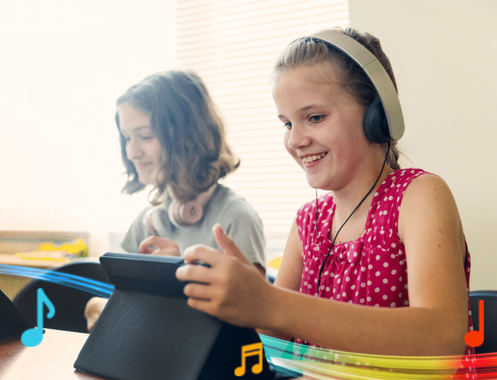 Two students are smiling, sitting next to each other and looking at their iPads. Both are wearing headphones.